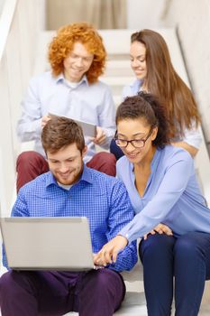 business, technology and startup concept - smiling creative team with laptop and tablet pc computer sitting on staircase