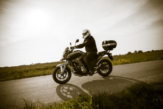 Biker in helmet and leather jacket riding on the road.