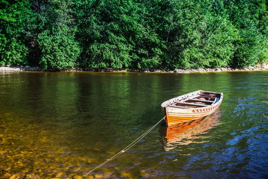 wooden boat on the river bank on forest background and blue sky reflecting in the surface of the river.
