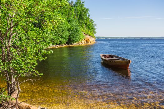 wooden boat on the river bank on forest background and blue sky reflecting in the surface of the river.