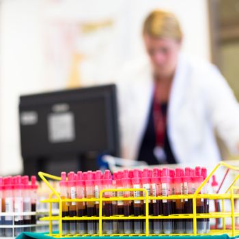 Rack of tubes with blood samples, laboratory technician working in the background.