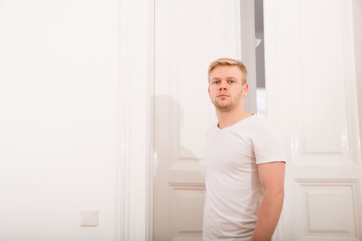 A young blonde man coming home passing through the door.