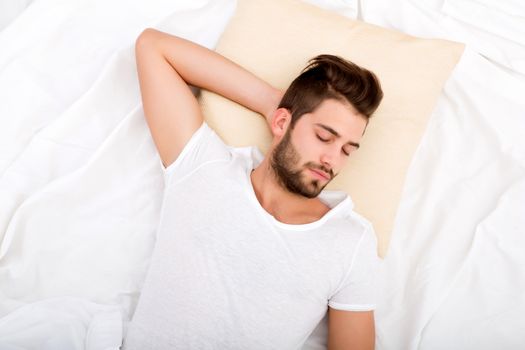 A handsome young adult man sleeping in bed.