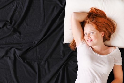 A young adult Woman lying on bed, smiling.
