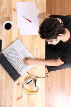 A young hispanic man working on a wooden desk with a laptop.