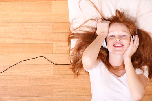 A young redhead girl lying on the floor while listening music.
