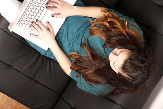 A young girl chatting on a laptop on the sofa.