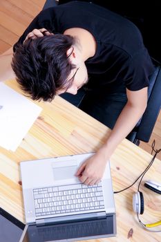 A young hispanic man working on a wooden desk with a laptop.