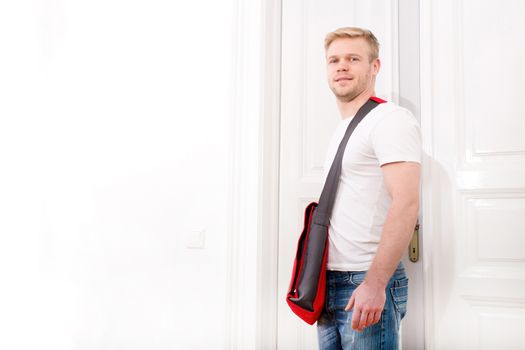 A young blonde man coming home passing through the door.
