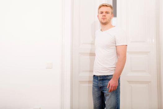 A young blonde man coming home passing through the door.