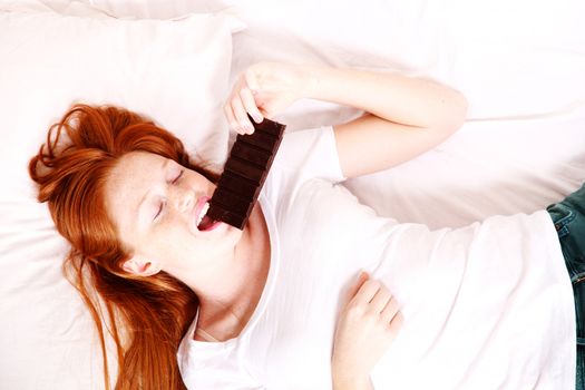 A young redhead woman eating Chocolate in Bed.