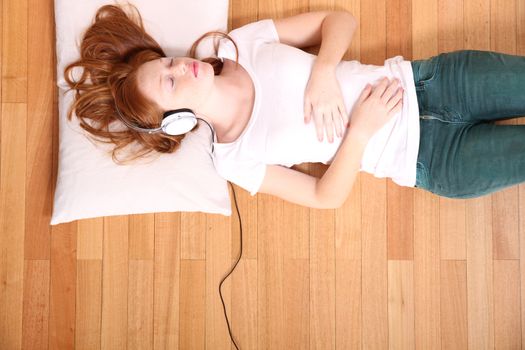 A young redhead girl lying on the floor while listening music.