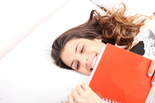 A young latin woman reading a book in bed.