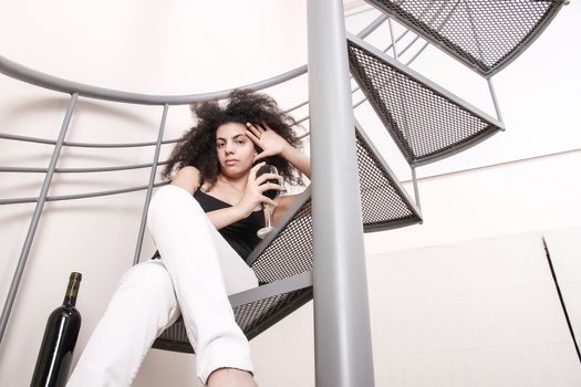 A young brazilian woman sitting on the stairs with a glass of red wine.