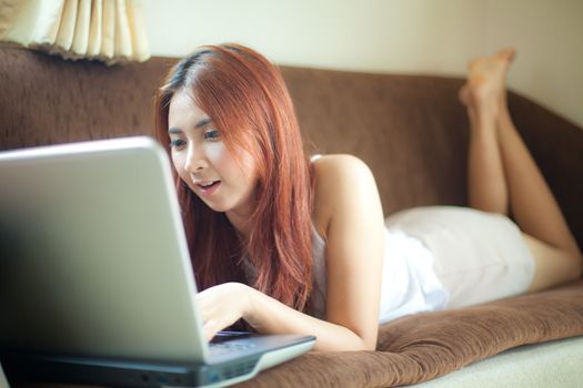 Happy asian young woman lying using laptop at home