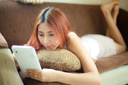 Happy asian young woman lying using tablet at home