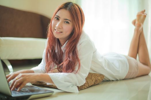 Happy asian young woman lying using laptop at home