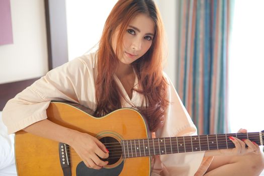 Young beautiful asian woman playing guitar in bed room