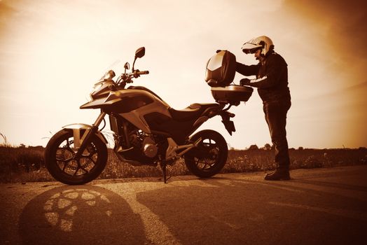 Biker standing with its motorbike on a misty sunset.