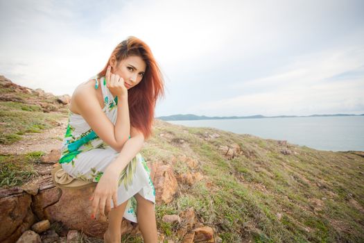 Young asian woman sitting on a cliff on the background of mountains and sea