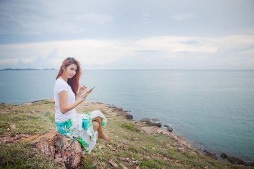 Young asian woman use tablet pc on mountain and sea