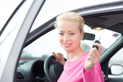 Woman driver showing car keys. Young female driving happy about her new car or drivers license. Caucasian model.