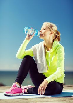 fitness and lifestyle concept - woman drinking water after doing sports outdoors