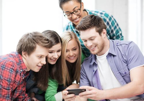 education and technology concept - group of students looking at smartphone at school