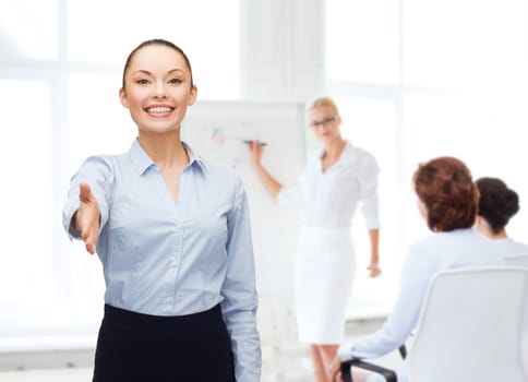 business, gesture and education concept - friendly young smiling businesswoman with opened hand ready for handshake