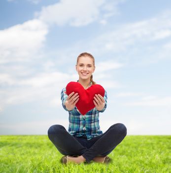 happiness and people concept - smiling young woman in casual clothes sitiing on floor and holding red heart