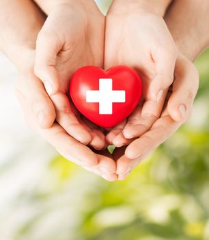 family health, charity and medicine concept - male and female hands holding red heart with cross sign