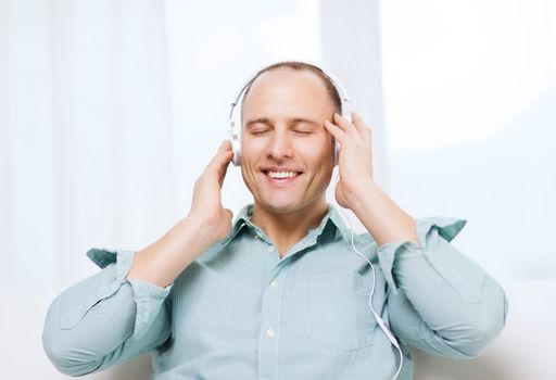 leisure and lifestyle concept - happy man with headphones listening to music at home