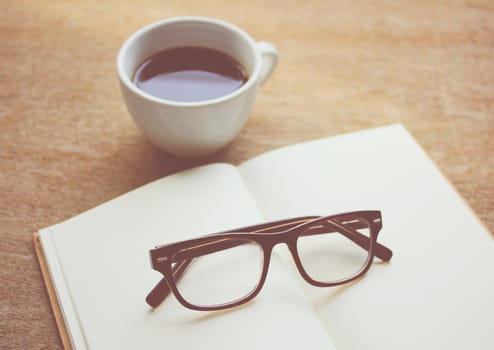 Eyeglasses on notebook and black coffee, retro filter effect