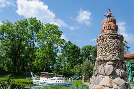 stylized stone brick lighthouse in the landscape summer park on blue sky background