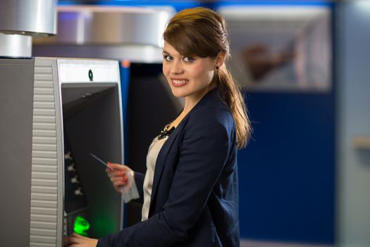 Pretty, young woman withdrawing money from her credit card in at an ATM (shallow DOF; color toned image)