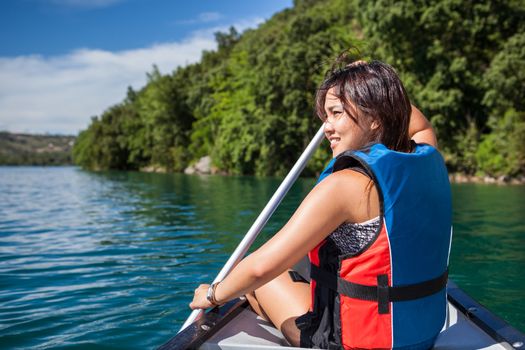 Pretty, young woman on a canoe on a lake, paddling, enjoying a lovely summer day