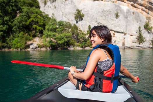 Pretty, young woman on a canoe on a lake, paddling, enjoying a lovely summer day