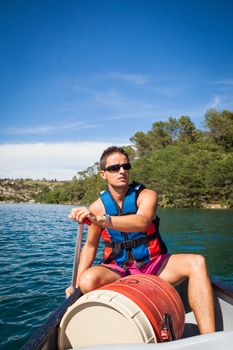 Handsome young man on a canoe on a lake, paddling, enjoying a lovely summer day