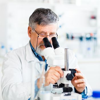 Senior male researcher carrying out scientific research in a lab using a microscope (shallow DOF; color toned image)