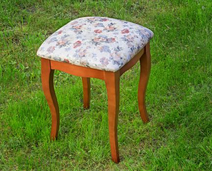 Beautiful stool in style of a retro with the soft seat upholstered with a gobelin. It is presented against a green lawn.