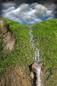 small waterfall over green moss and blue sky background