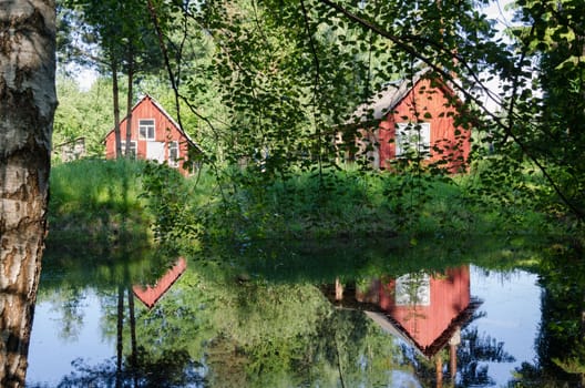 two small red rural home reflected through birch branches on pond