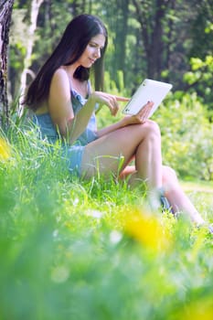 Young woman using tablet outdoor sitting green grass with flowers