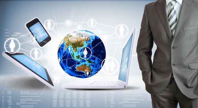 Businessman with the earth and electronics. High-tech graphs at backdrop. Elements of this image are furnished by NASA
