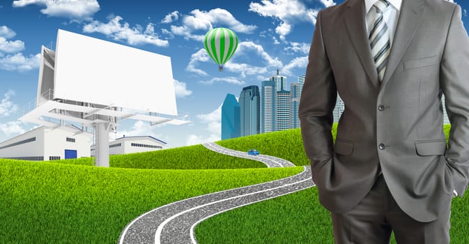 Businessman standing with hands in pockets. Blank billboard, road, skyscrapers and industrial area as backdrop