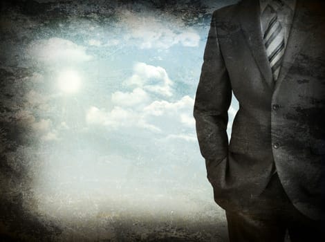 Businessman standing with hands in pockets. Blue sky and white clouds as backdrop. Grunge style