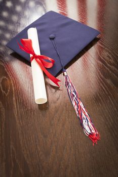 Graduation Cap with Tassel and Diploma Wresting on Wooden Table with American Flag Reflection.