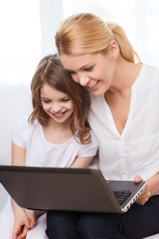 family, child, technology and home concept - smiling mother and little girl with laptop at home