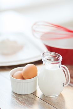 cooking and food concept - close up of jugful of milk, eggs in a bowl and flour