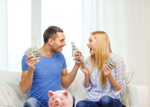 love, family, finance, money and happiness concpet - smiling couple with money and piggybank ot table at home